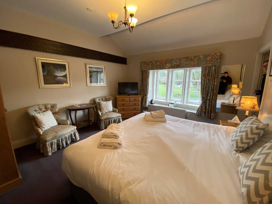 A hotel room with a large bed, two armchairs, a small table, a TV, and a window with curtains.
