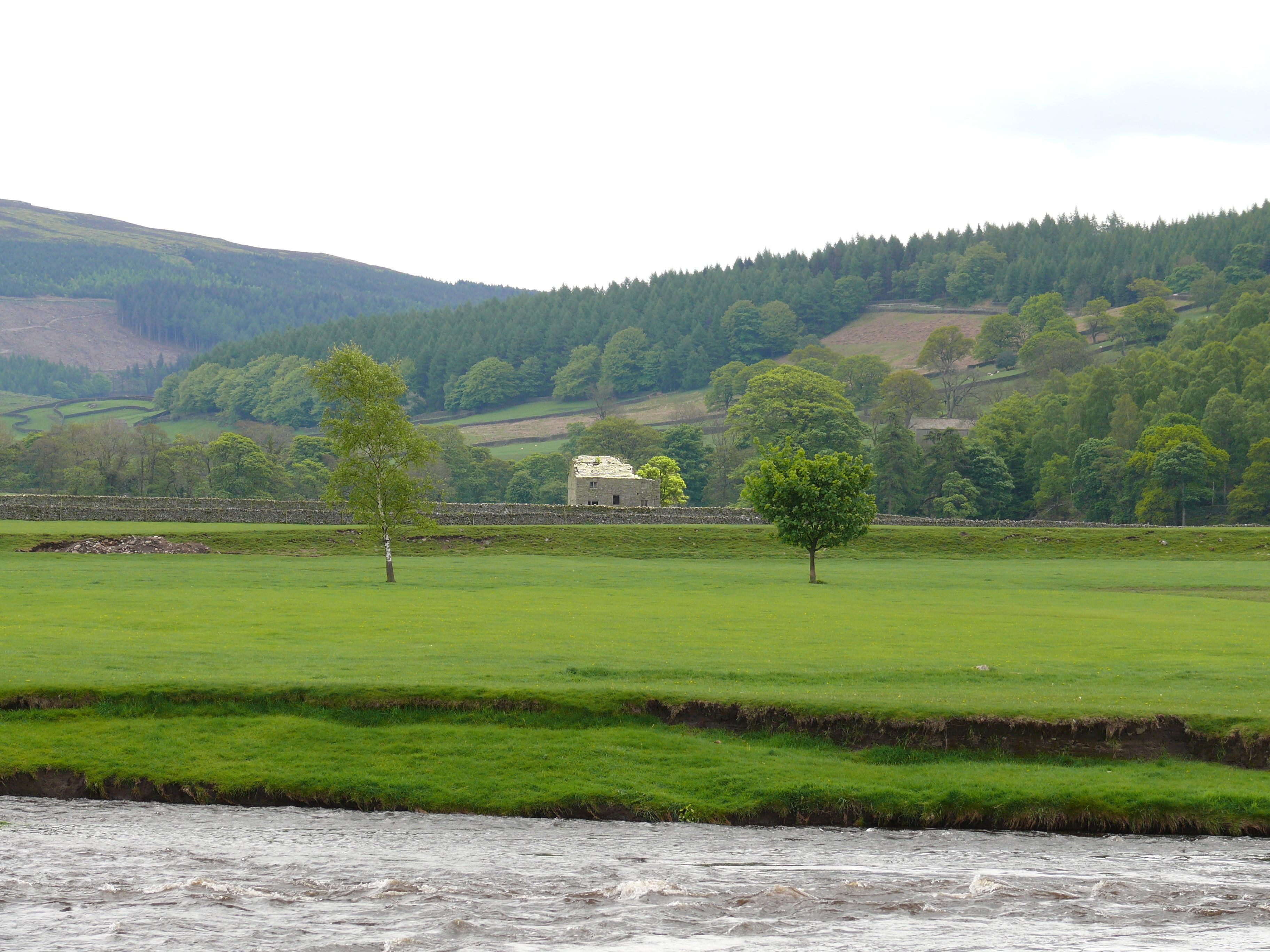 Ländliche Landschaft mit einem Steinhaus, grünen Feldern und einem Fluss.