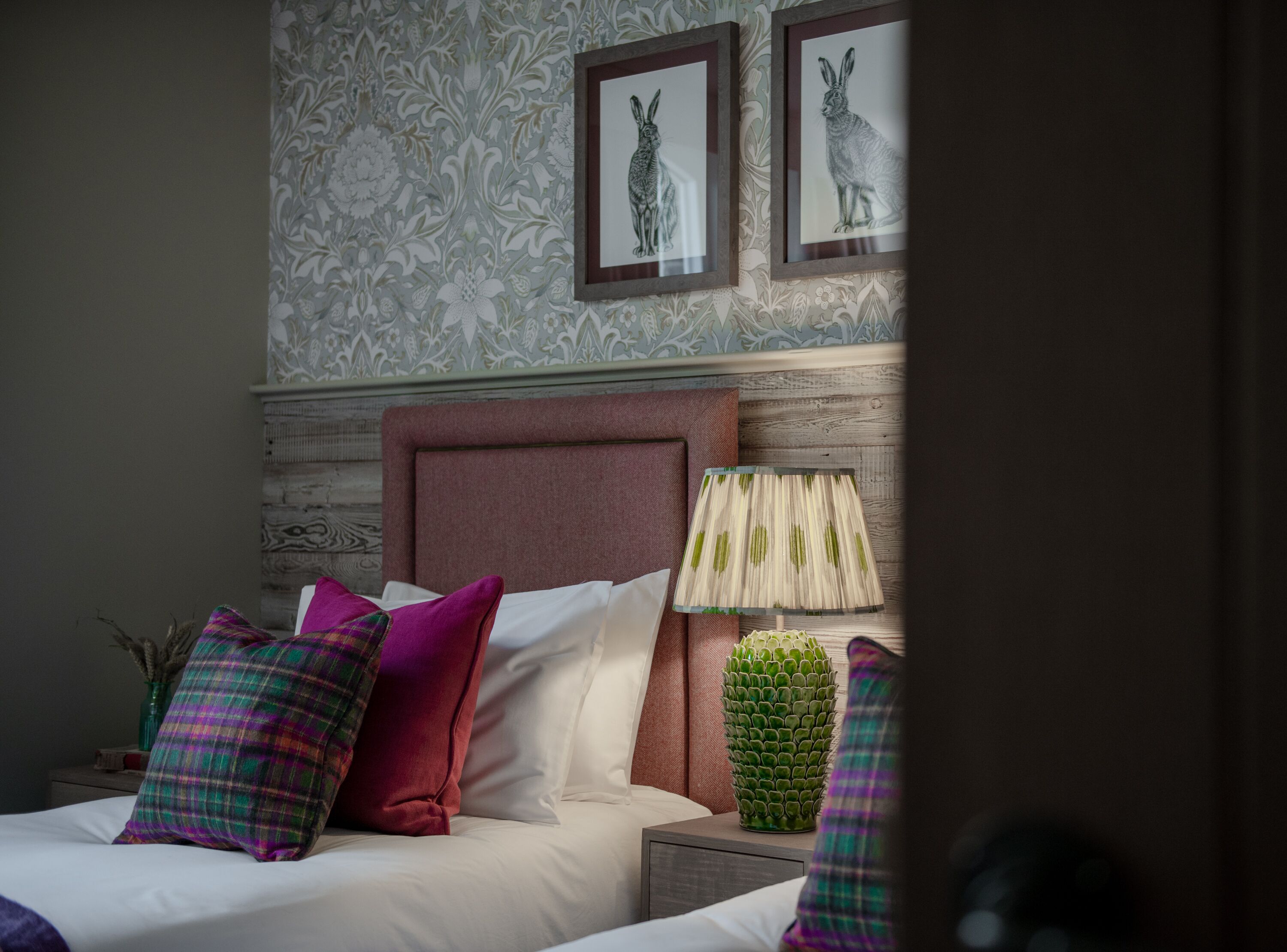 A neatly made bed with multiple pillows, a headboard, a lamp, and a decorative plant on a nightstand.