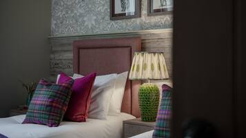 A neatly made bed with multiple pillows, a headboard, a lamp, and a decorative plant on a nightstand.