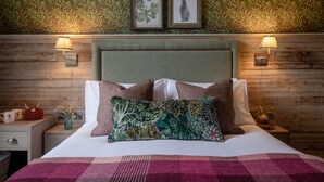 A neatly made bed with a floral pillow, a wooden headboard, and two wall-mounted lamps. - Red Lion Hotel and Manor House (Skipton)