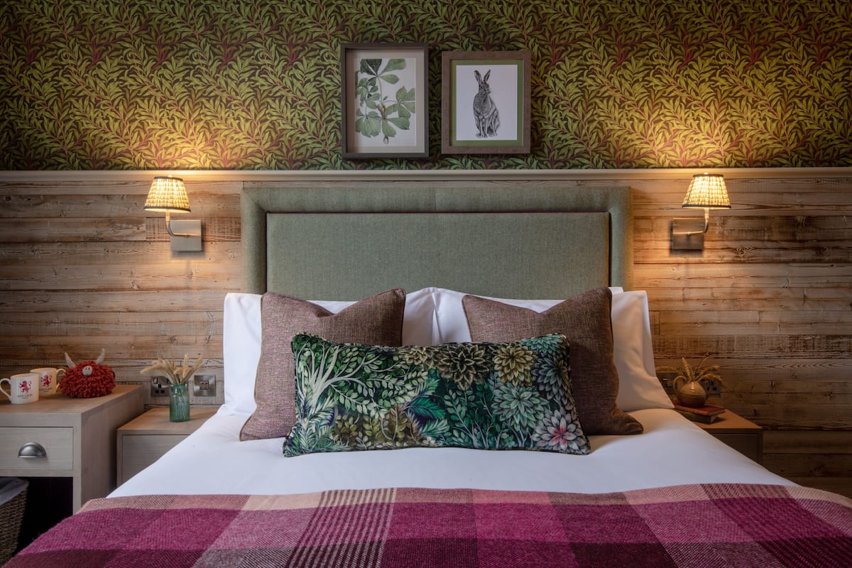 A neatly made bed with a floral pillow, a wooden headboard, and two wall-mounted lamps.