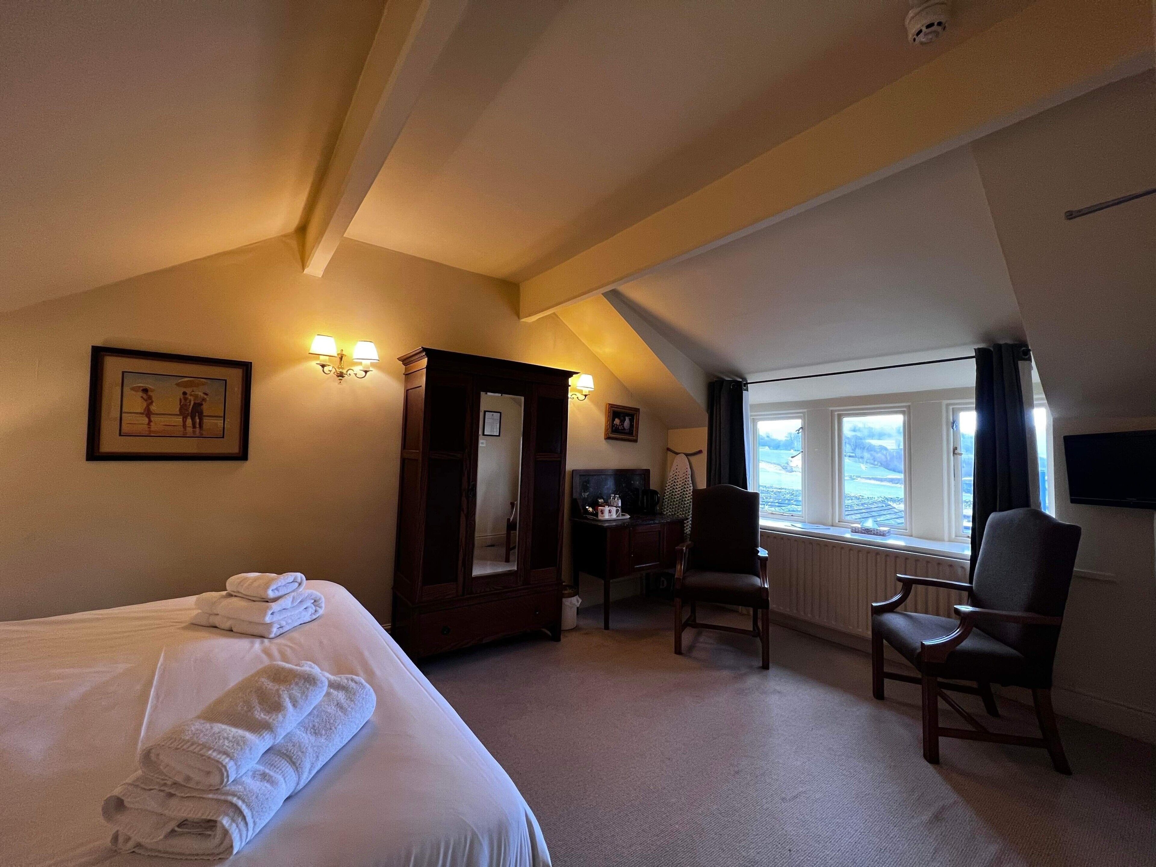 Une chambre d’hôtel avec un lit, une chaise, un bureau, une armoire et une fenêtre donnant sur un paysage agréable.