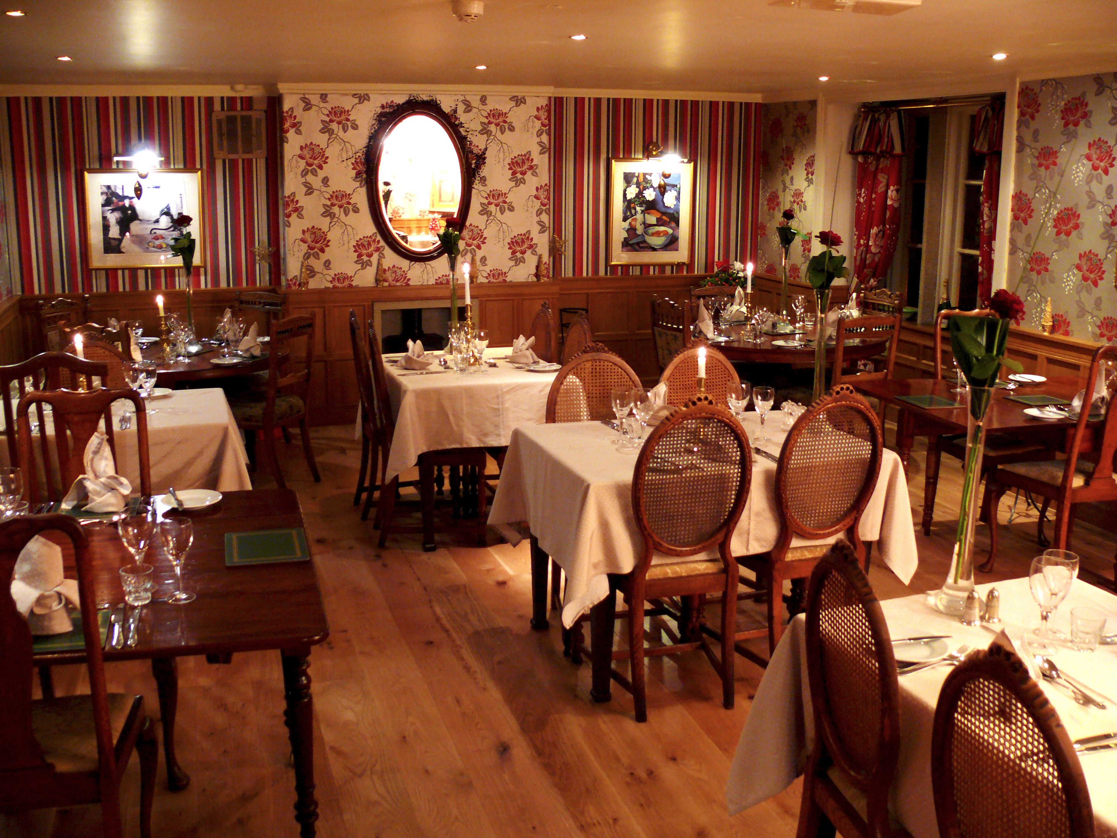 A dining area with multiple tables set for meals, wooden chairs, and floral wallpaper.