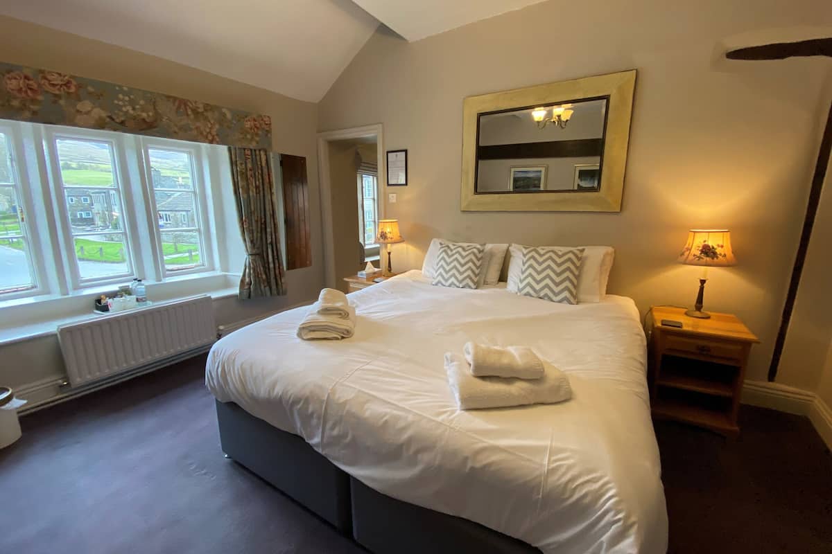 A neatly made bed with towels, a bedside lamp, and a window with curtains.