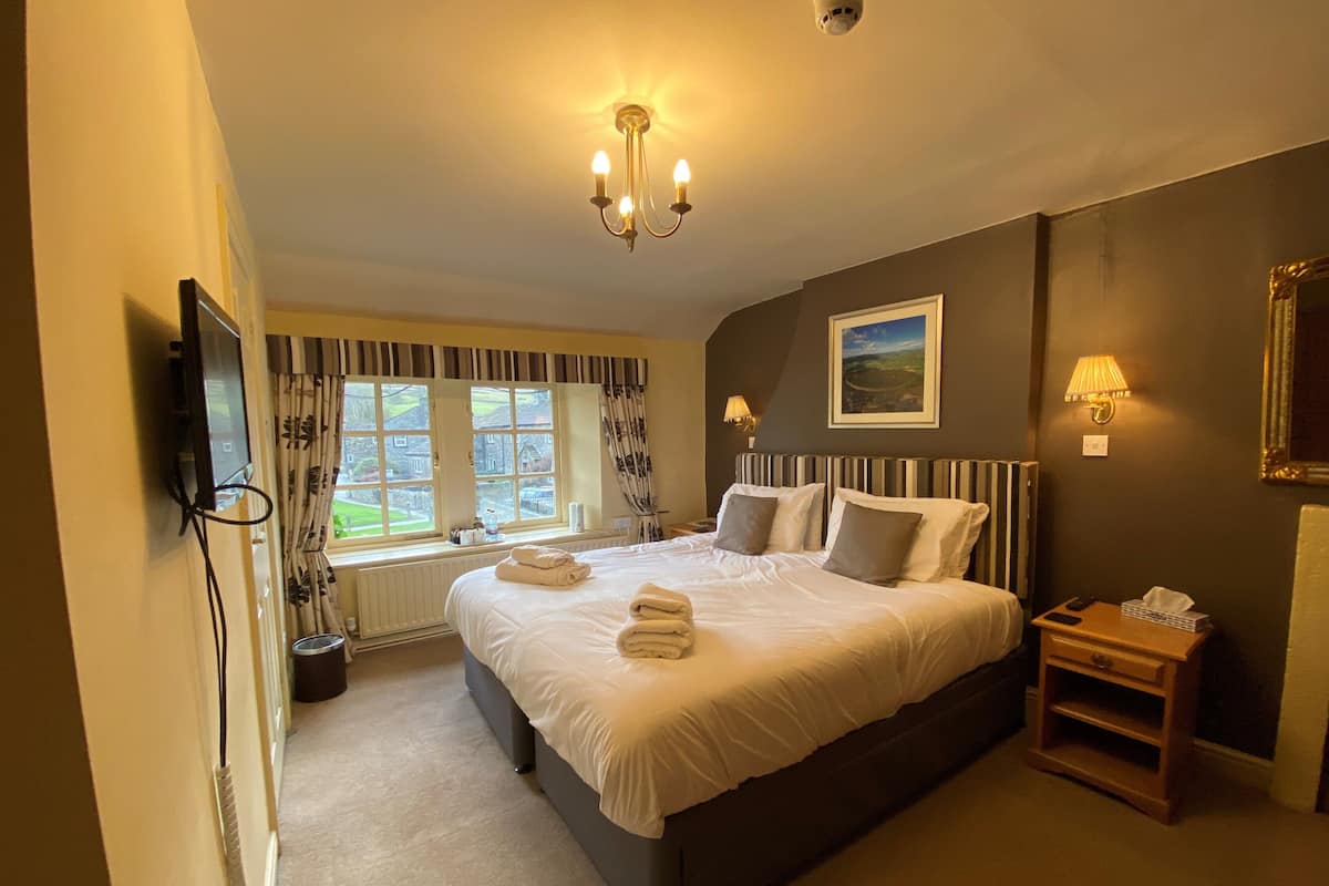 A bedroom with a large bed, a television mounted on the wall, a window with curtains, and a ceiling light fixture.