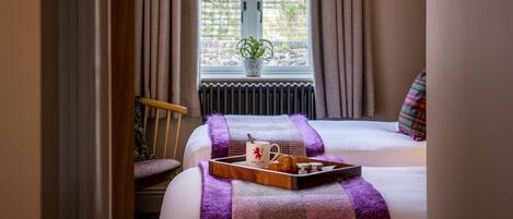 Ein Schlafzimmer mit Bett, einem Fenster mit Vorhängen, einem Stuhl und einem Tablett mit Gegenständen auf dem Bett.