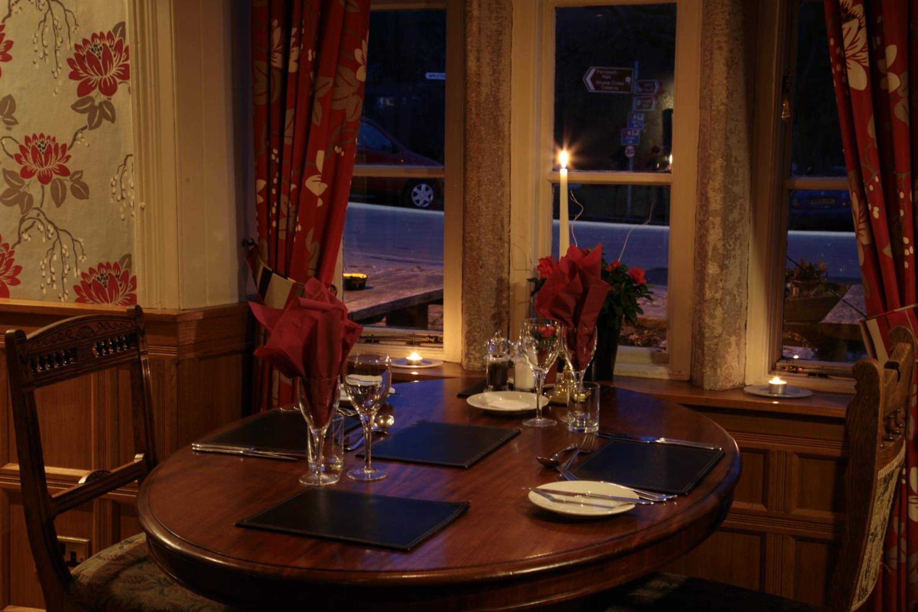A dining table set for two with a candle, wine glasses, and a vase of flowers.