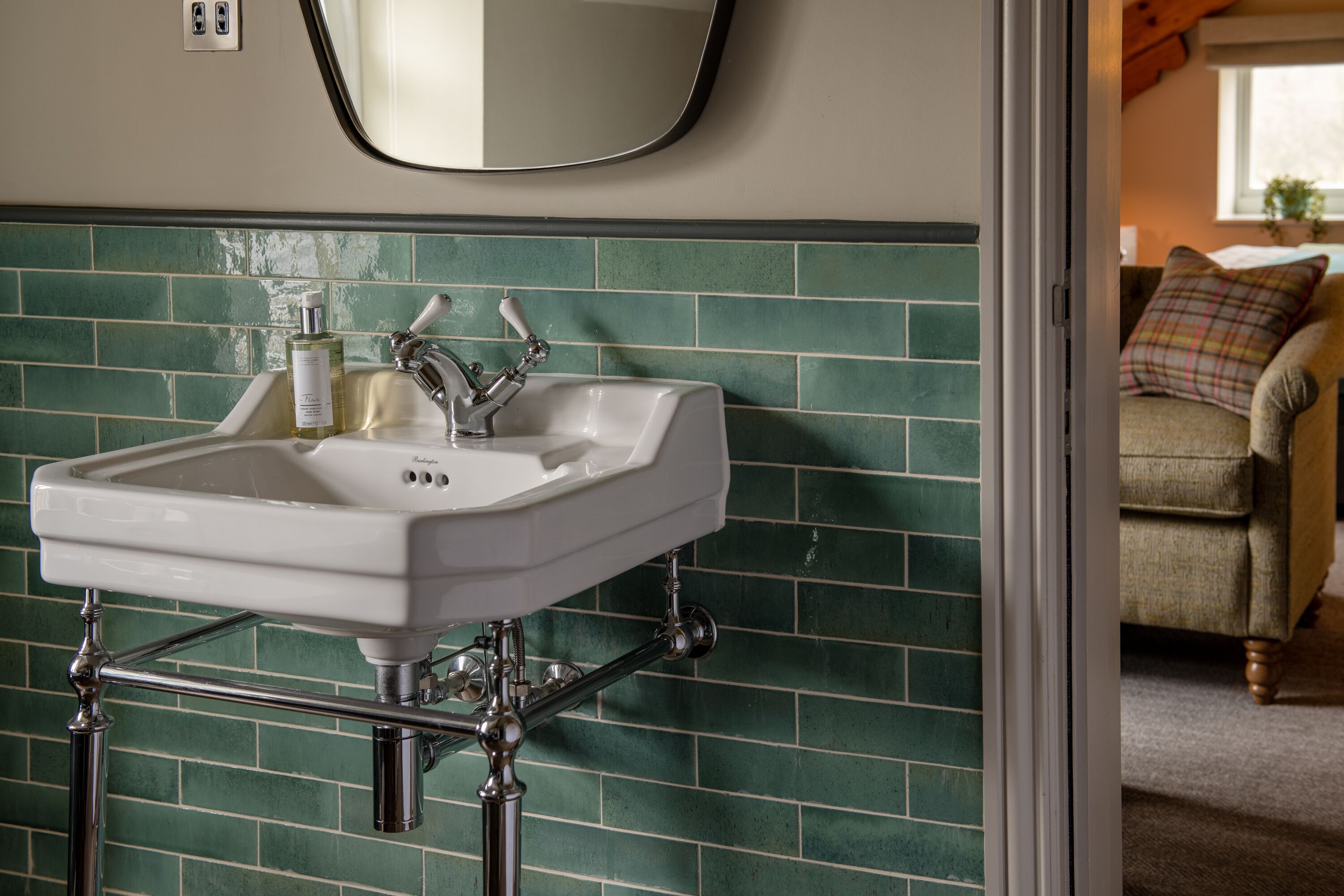 Un baño con un lavabo blanco, paredes cubiertas de azulejos verdes y un espejo sobre el lavabo.