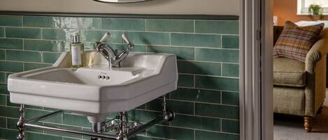 Un baño con un lavabo blanco, paredes cubiertas de azulejos verdes y un espejo sobre el lavabo.