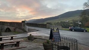 A stone bridge, a signboard for Theakston, and a car on a wet road. - Red Lion Hotel and Manor House (Skipton)