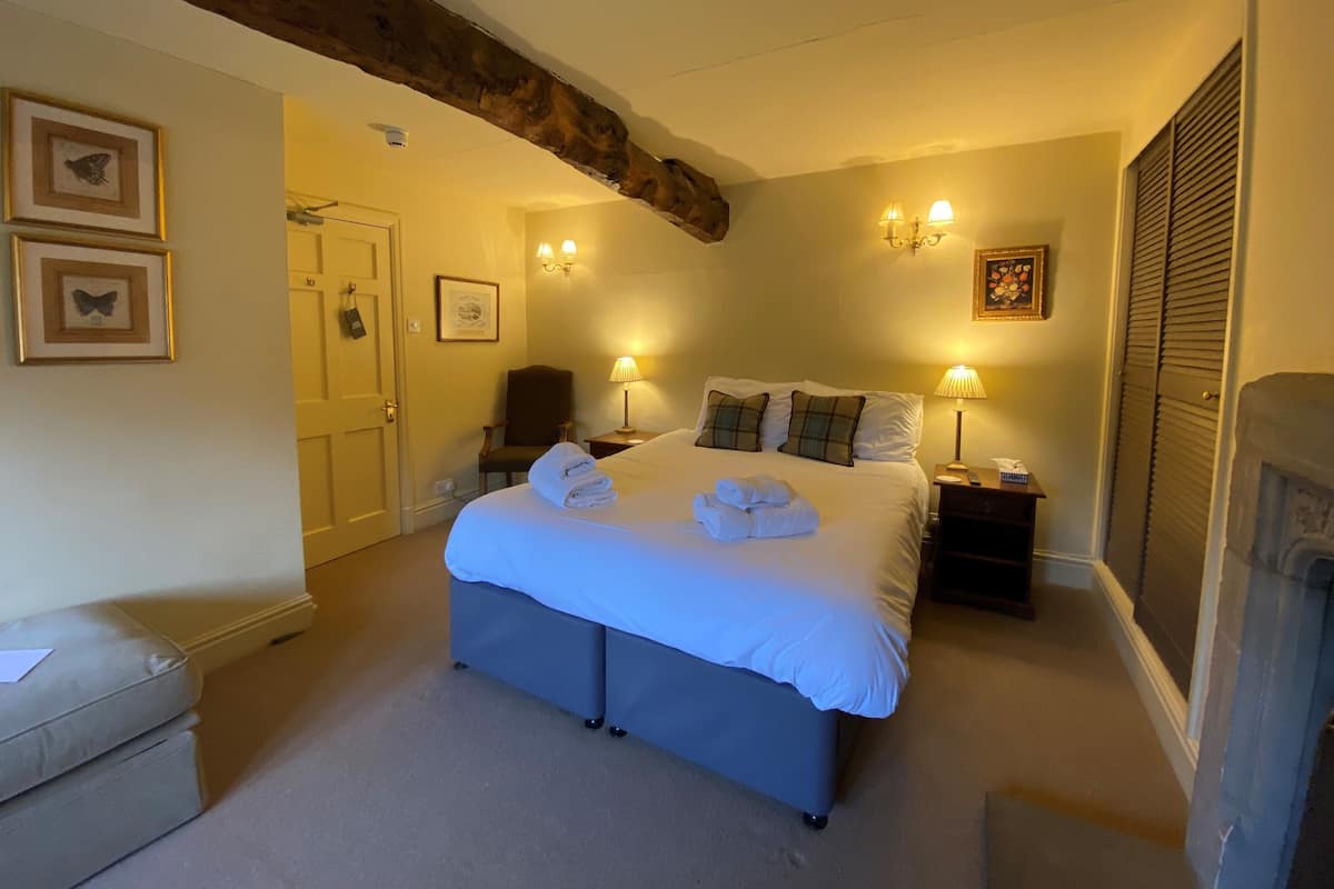 A bedroom with a large bed, two bedside lamps, a chair, and a fireplace.