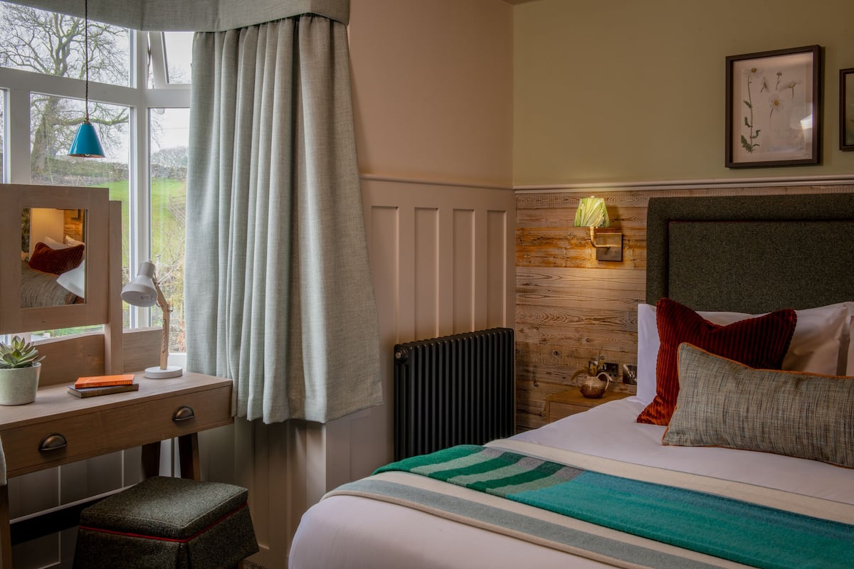 A bedroom with a bed, a desk with a chair, a radiator, and a window with curtains.