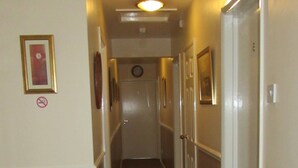 A narrow hallway with beige walls, a carpeted floor, and doors on both sides leading to rooms. There is a no-smoking sign on the left wall and a framed picture above a door. - OYO 4 Sisters Inn (Lincoln)