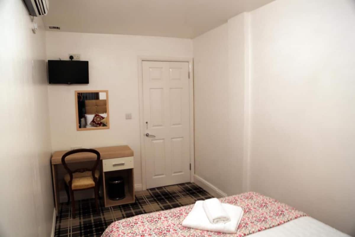 A bedroom with a bed, a desk, a chair, a door, and a mounted television.