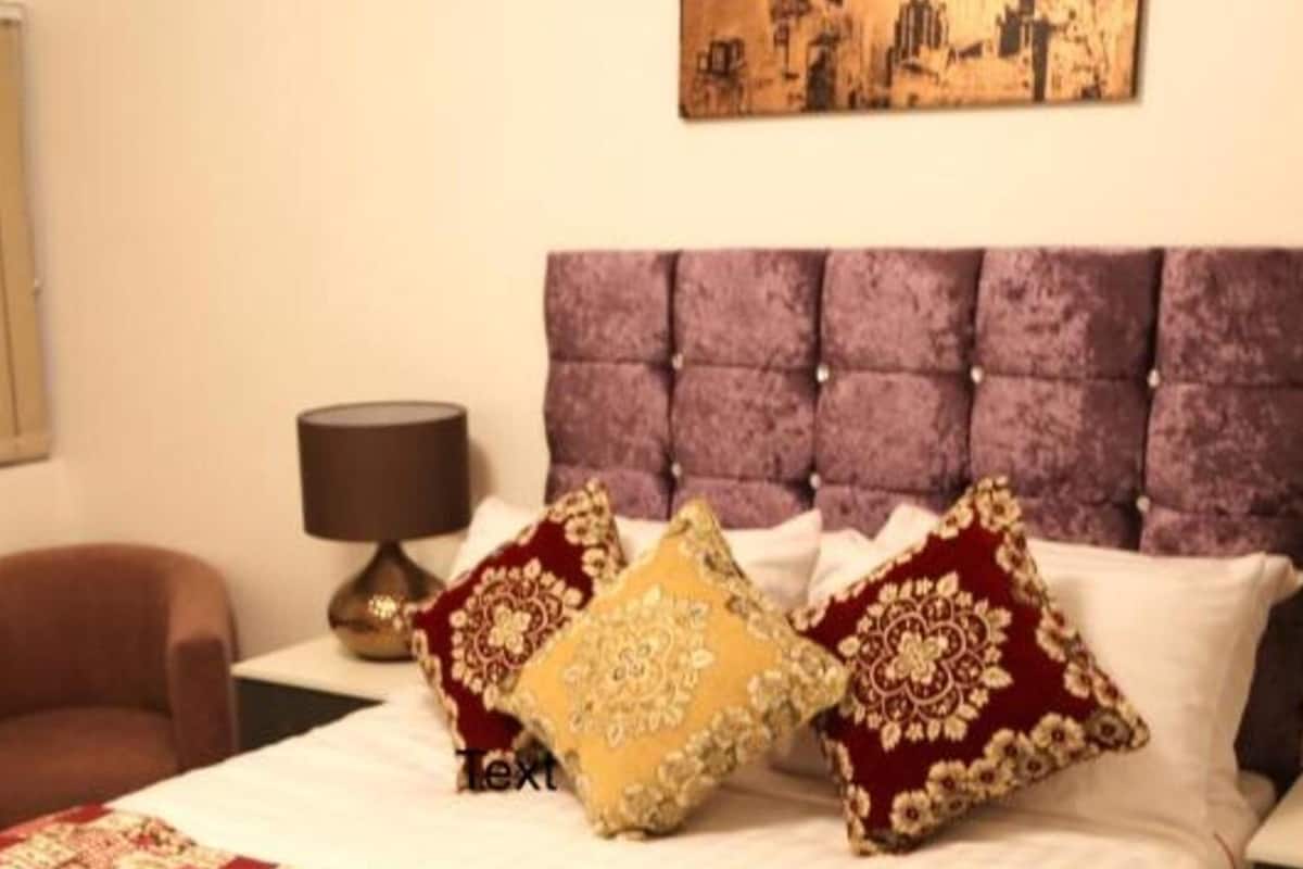 A hotel room with a tufted headboard, a brown armchair, and decorative pillows.
