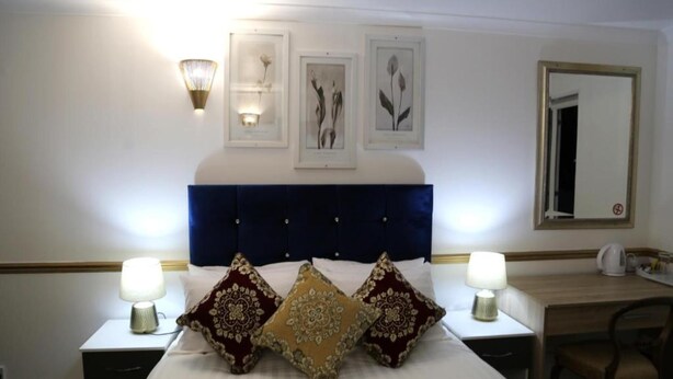 A hotel room with a large bed, two bedside tables with lamps, a desk, and a chair. There are three framed botanical prints on the wall above the bed. - OYO 4 Sisters Inn (Lincoln)