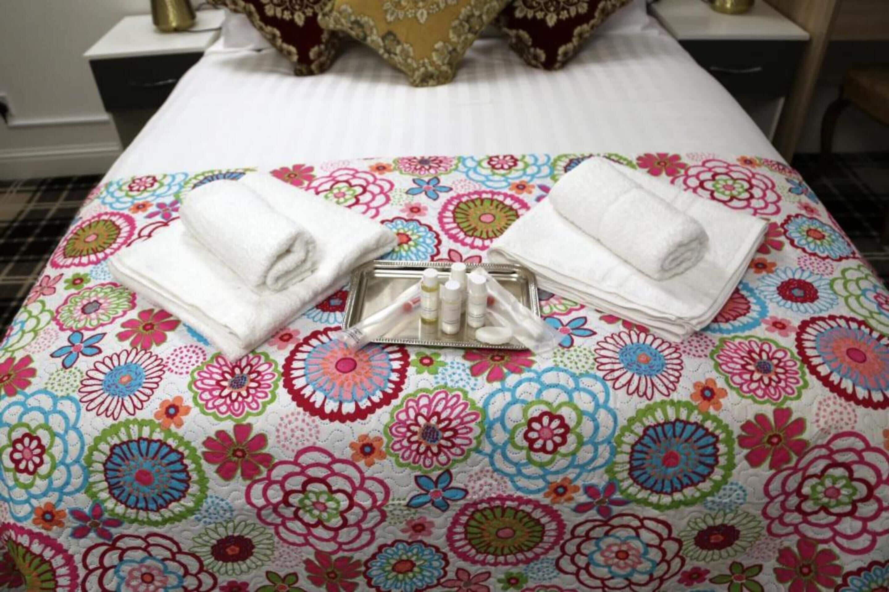 A bed with a colorful floral bedspread, two neatly folded white towels, and a tray with toiletries.