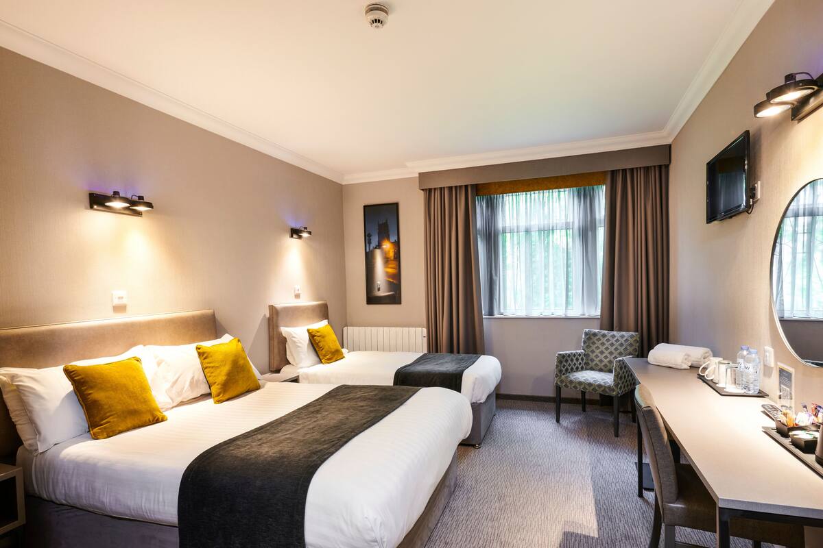 A hotel room with two beds, a desk, a chair, and a large window with curtains.