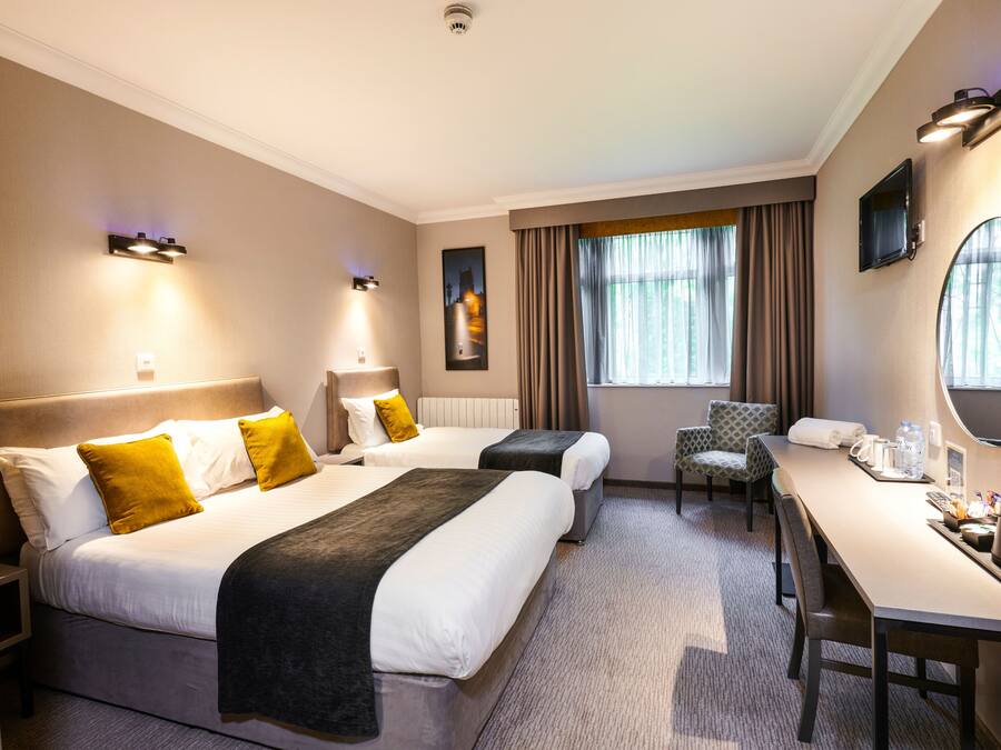 Hotelkamer met twee bedden, een bureau, een stoel en een groot raam met gordijnen.