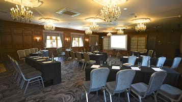 A conference room with multiple tables and chairs, chandeliers, and a projector screen displaying "THE ROYAL TOWER".