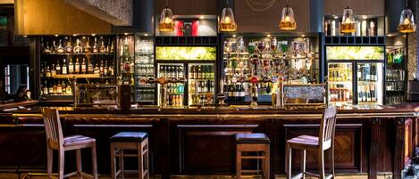 A bar area with wooden bar stools, a well-stocked liquor shelf, and hanging pendant lights.