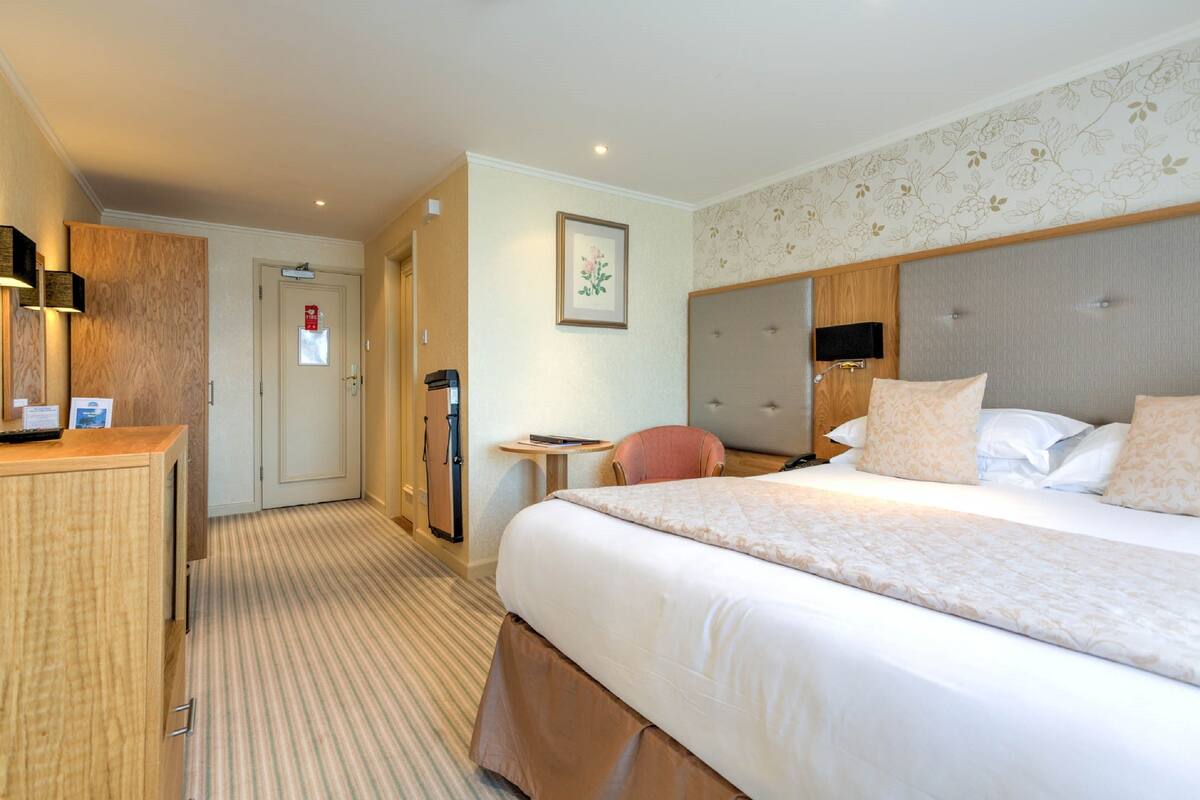 Une chambre d’hôtel avec un grand lit, un bureau, une chaise, une petite table et une armoire.