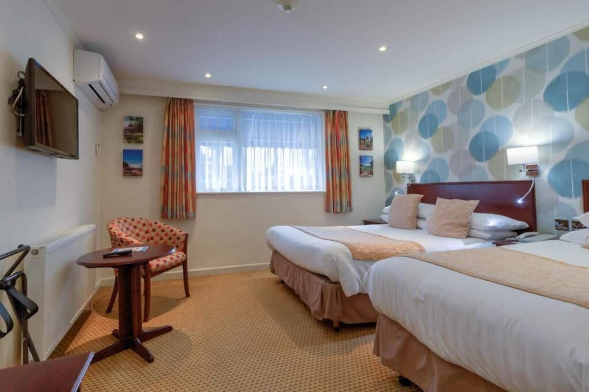 Une chambre d’hôtel avec deux lits, une télévision, une chaise, une petite table et une fenêtre avec des rideaux.