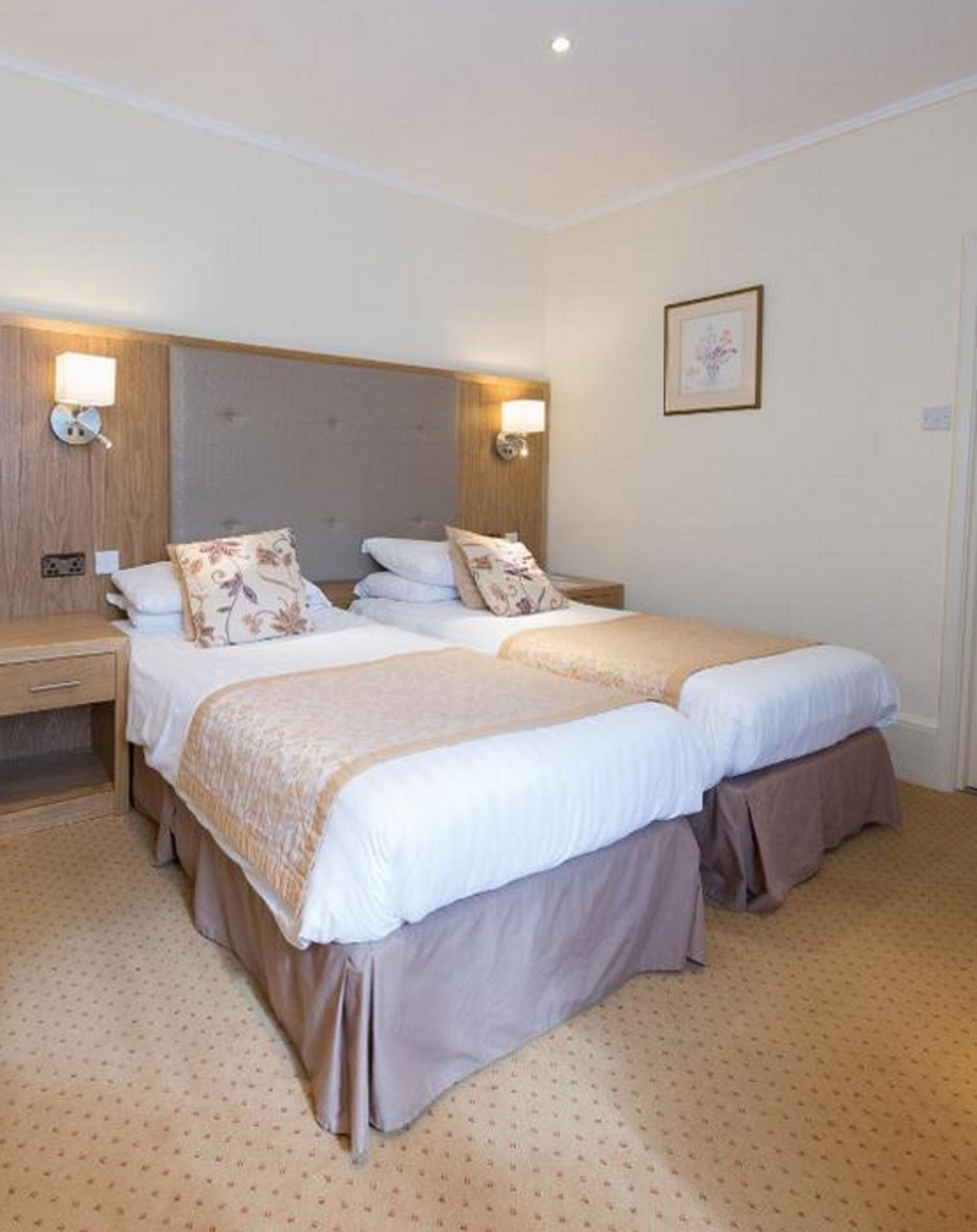 A double room with two beds, each with a headboard, bedside tables, and wall-mounted lamps.