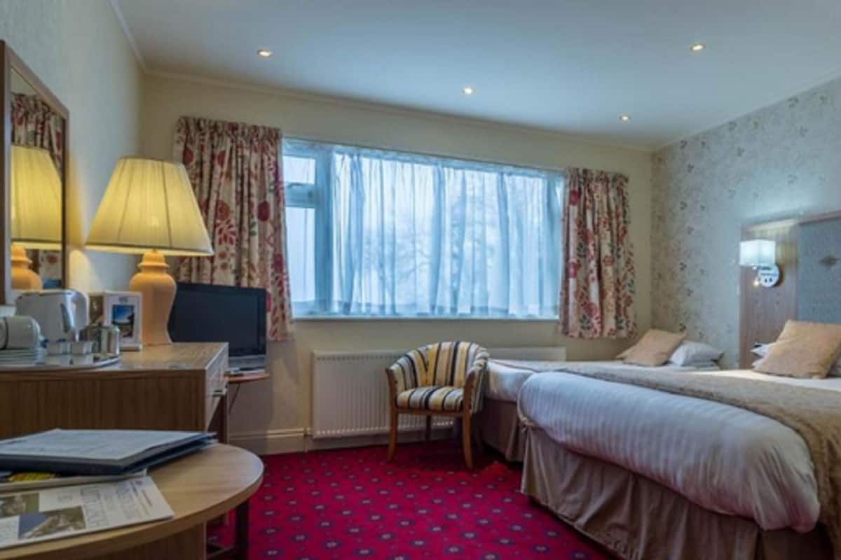Une chambre d’hôtel avec un lit, un bureau doté d’une lampe, une chaise et une fenêtre avec des rideaux.