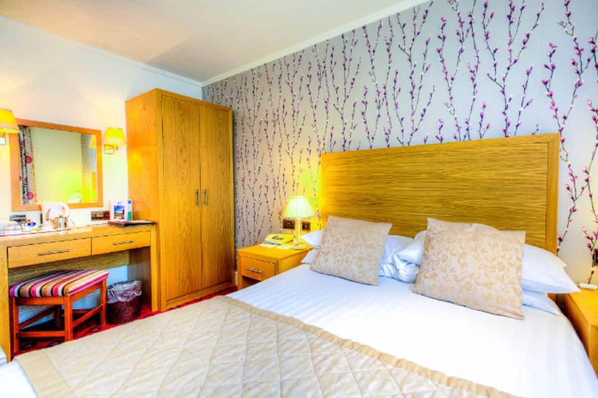 Une chambre d’hôtel avec un grand lit, une armoire en bois, une table de chevet avec une lampe et un petit tabouret.