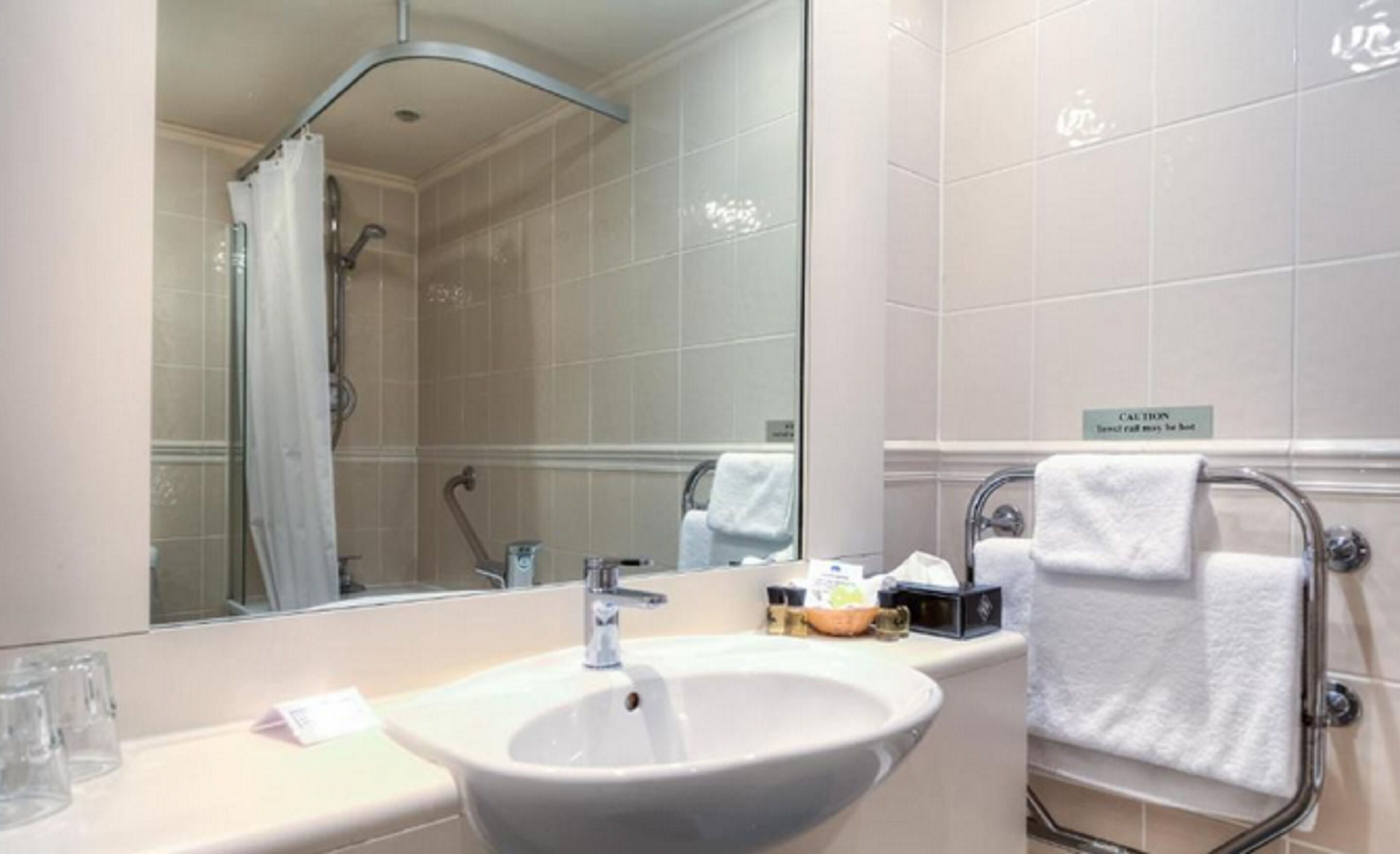 A hotel bathroom with a sink, mirror, shower, and towel rack.
