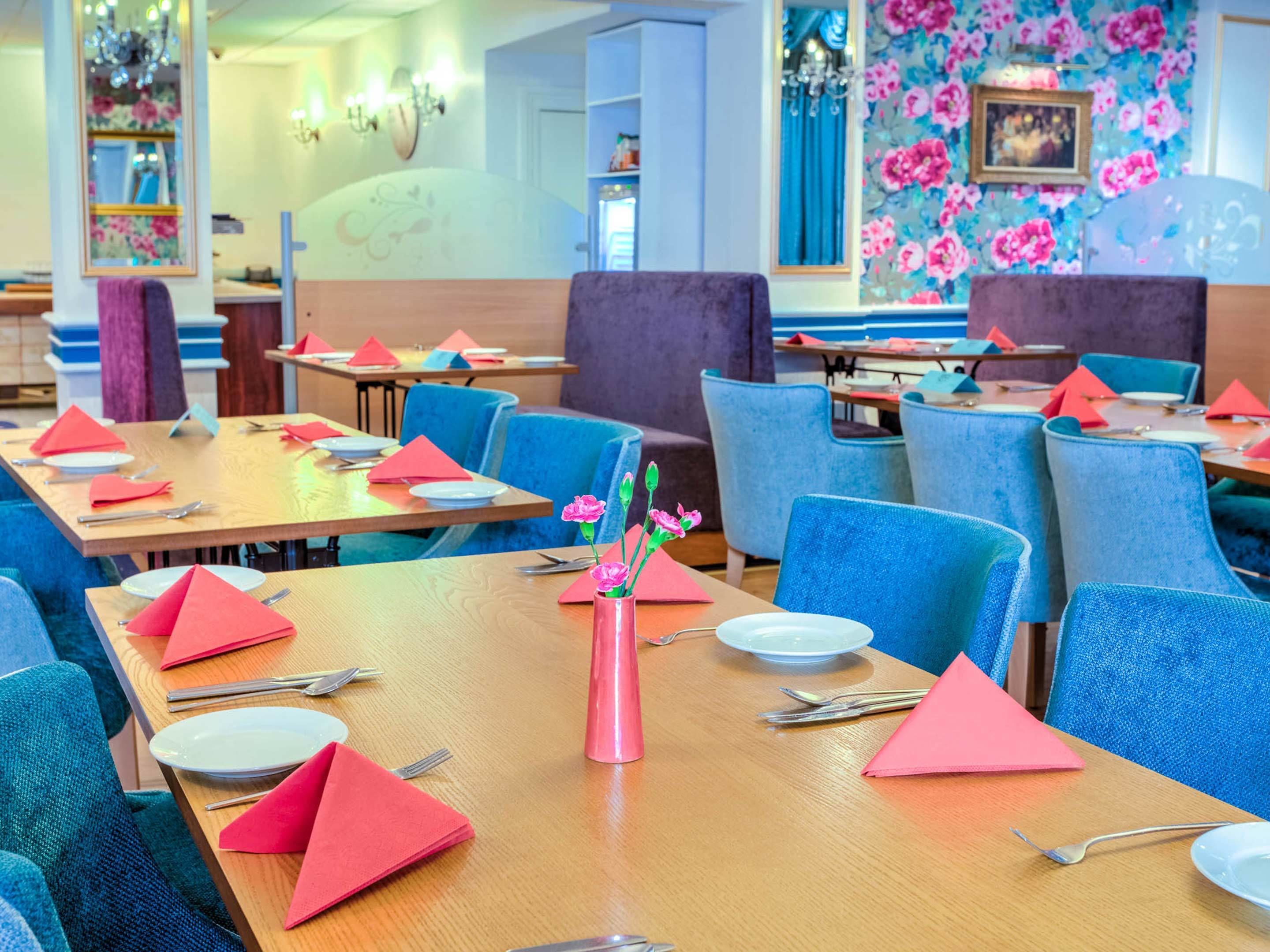 Un restaurant avec des chaises bleues, des tables en bois et des serviettes rouges.