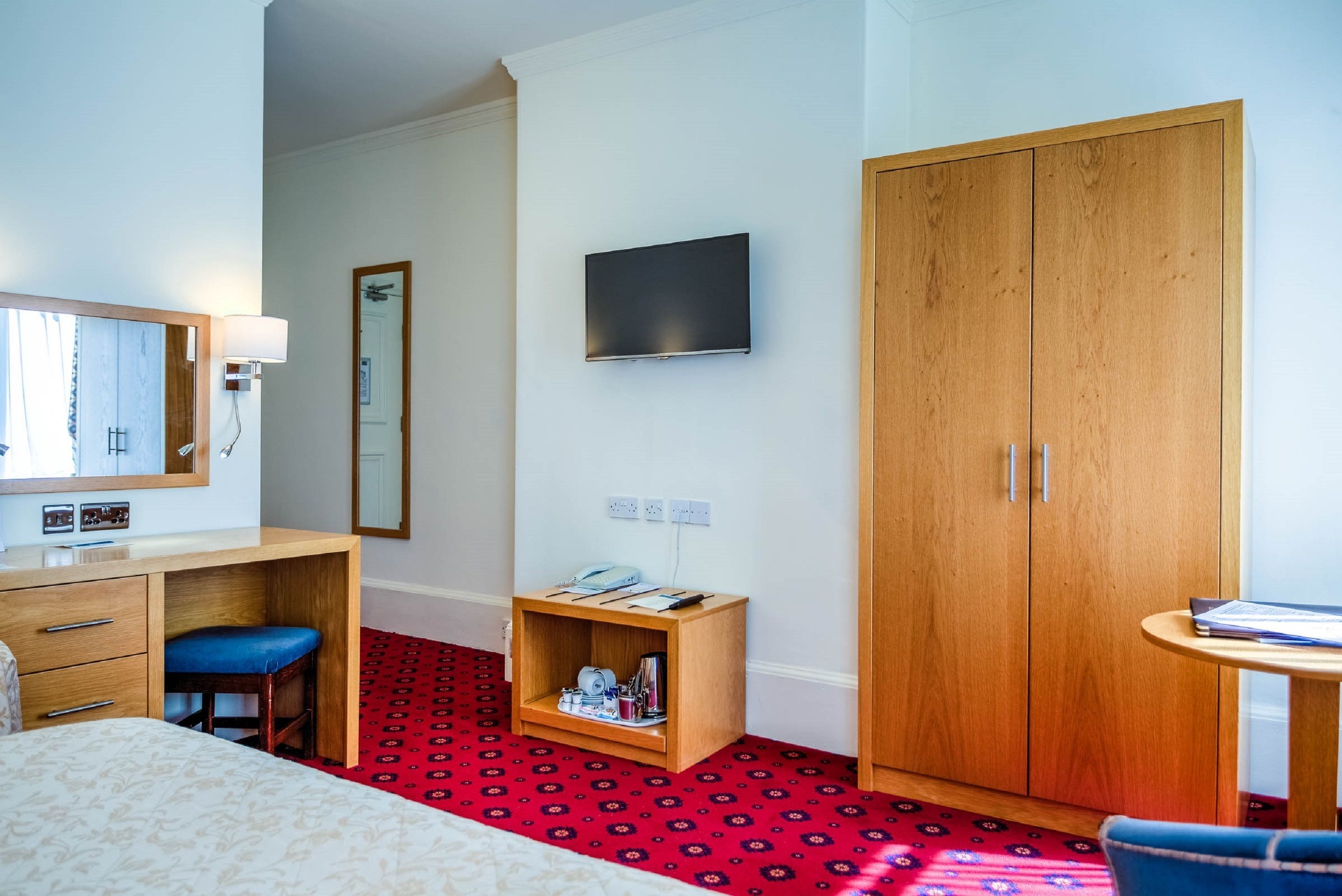 Een hotelkamer met een bed, een bureau, een stoel, een kledingkast, een televisie en een klein plankje met spullen.