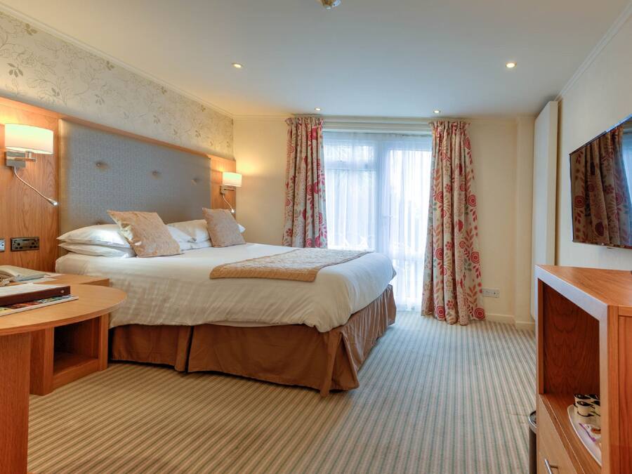 Ein Hotelzimmer mit einem großen Bett, einem Nachttisch, einem Schreibtisch, einem Fernseher und einem Fenster mit Vorhängen.