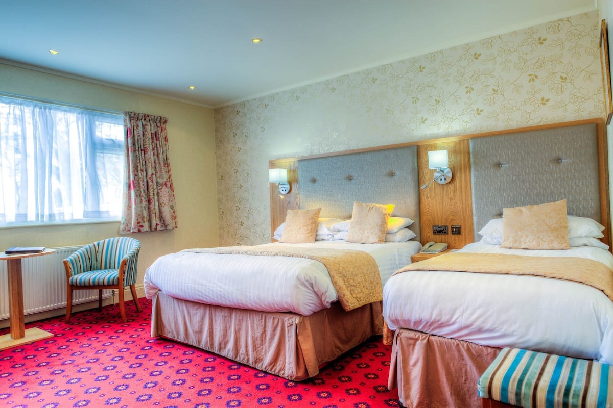 Une chambre d’hôtel avec deux lits, une chaise, une petite table et une fenêtre avec des rideaux.