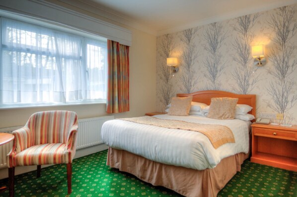 Habitación de hotel con una cama grande, una silla, una mesita de noche y una ventana con cortinas.