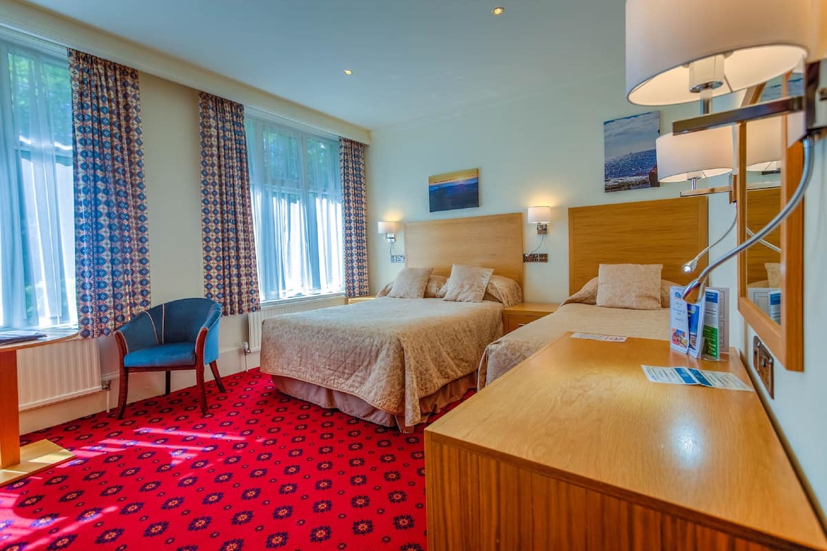 Une chambre d’hôtel avec deux lits, un bureau, une chaise et une grande fenêtre avec des rideaux.