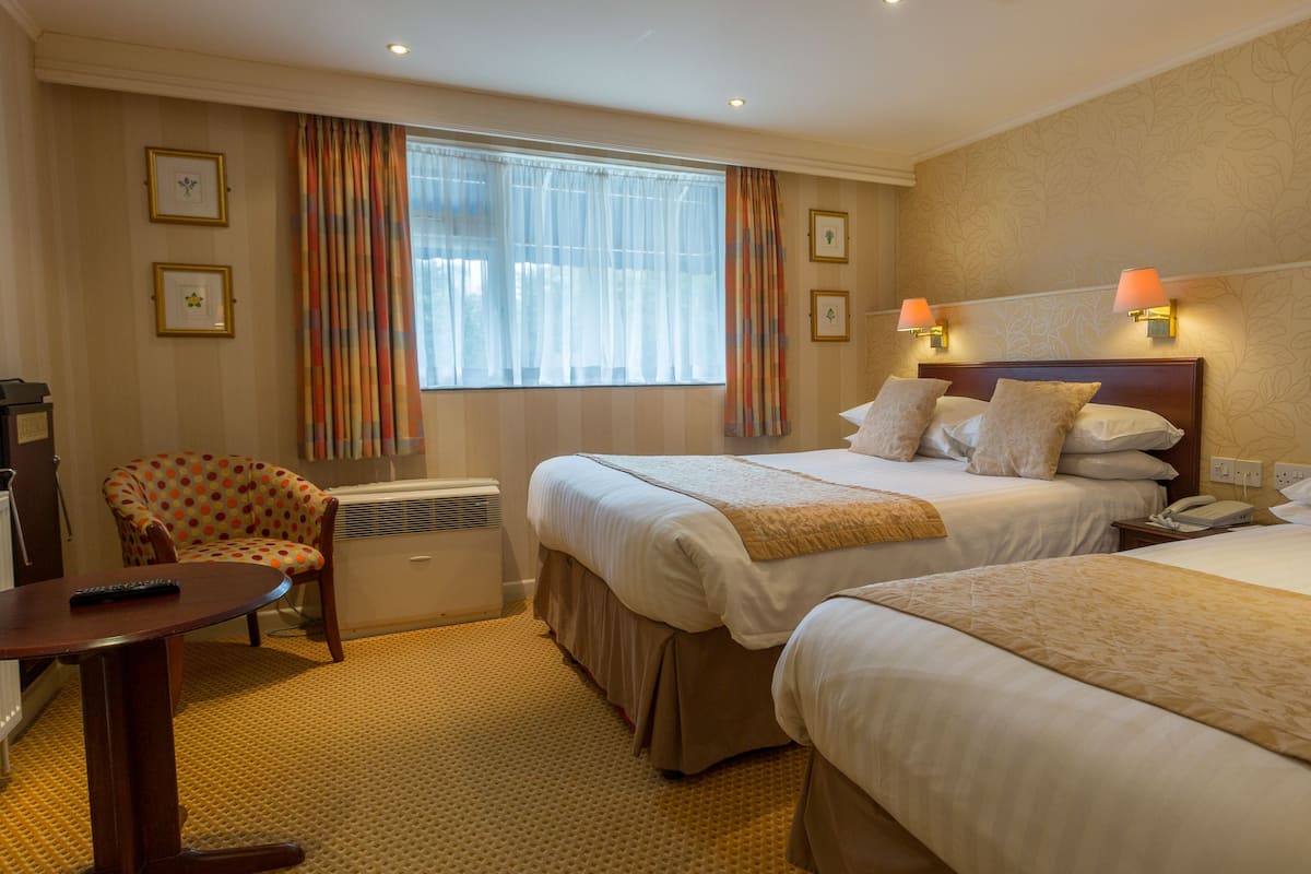 Une chambre d’hôtel avec deux lits, un bureau, une chaise et un radiateur.