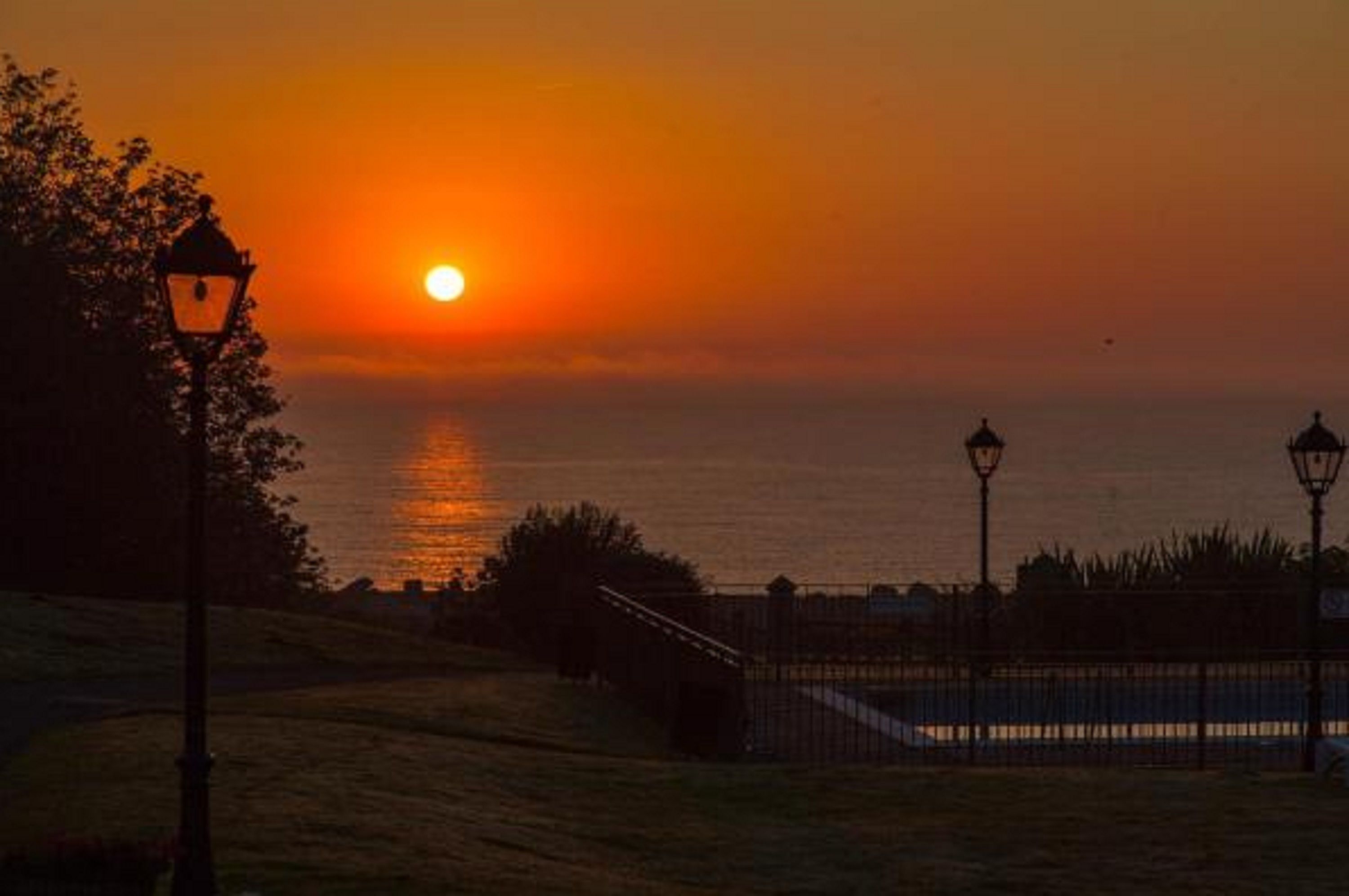 A sunset over a body of water with a lamp post and a fence in the foreground.