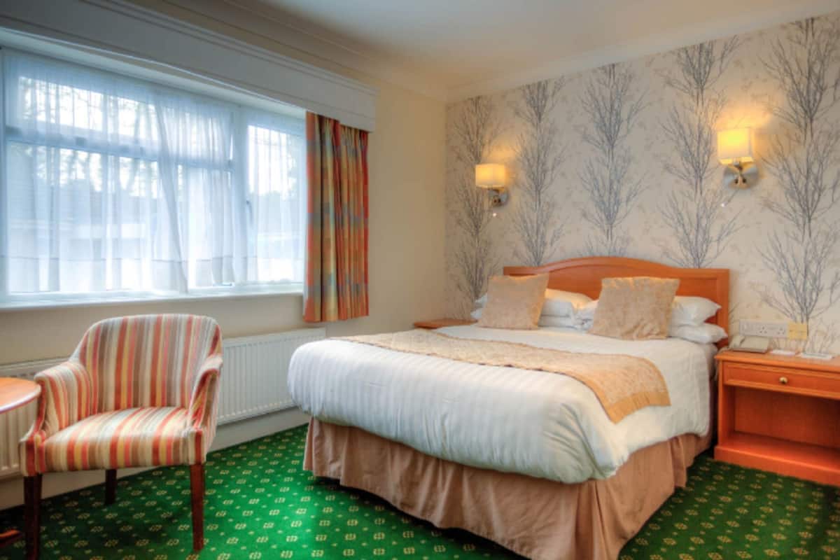 Une chambre d’hôtel avec un lit, une chaise, une table de chevet et une fenêtre avec des rideaux.