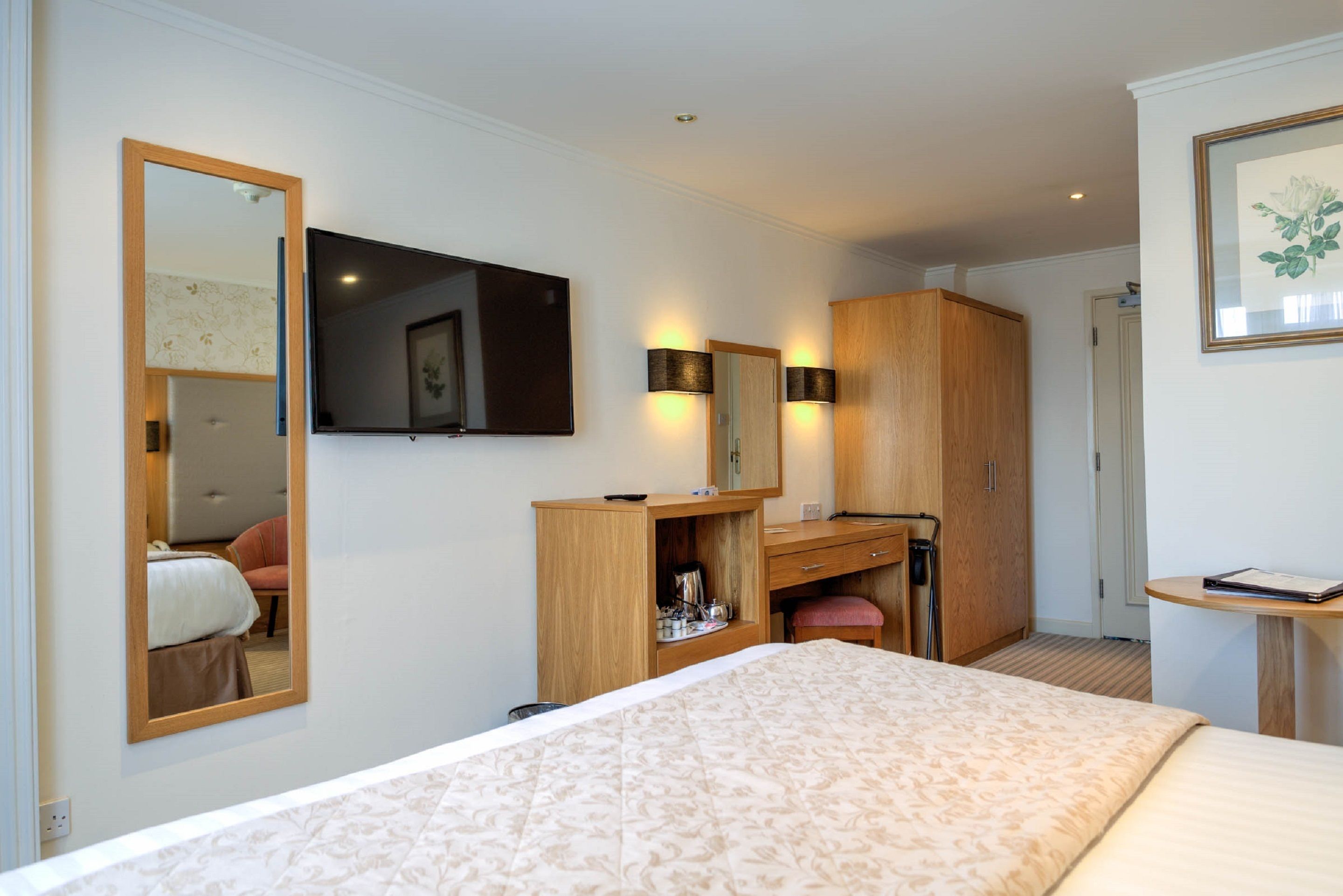 Habitación de hotel con una cama grande, un escritorio con silla, armario, espejo y televisión en la pared.