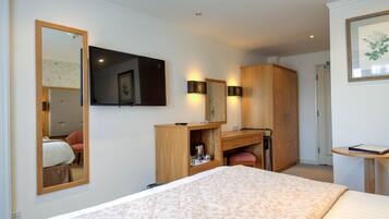Habitación de hotel con una cama grande, un escritorio con silla, armario, espejo y televisión en la pared.