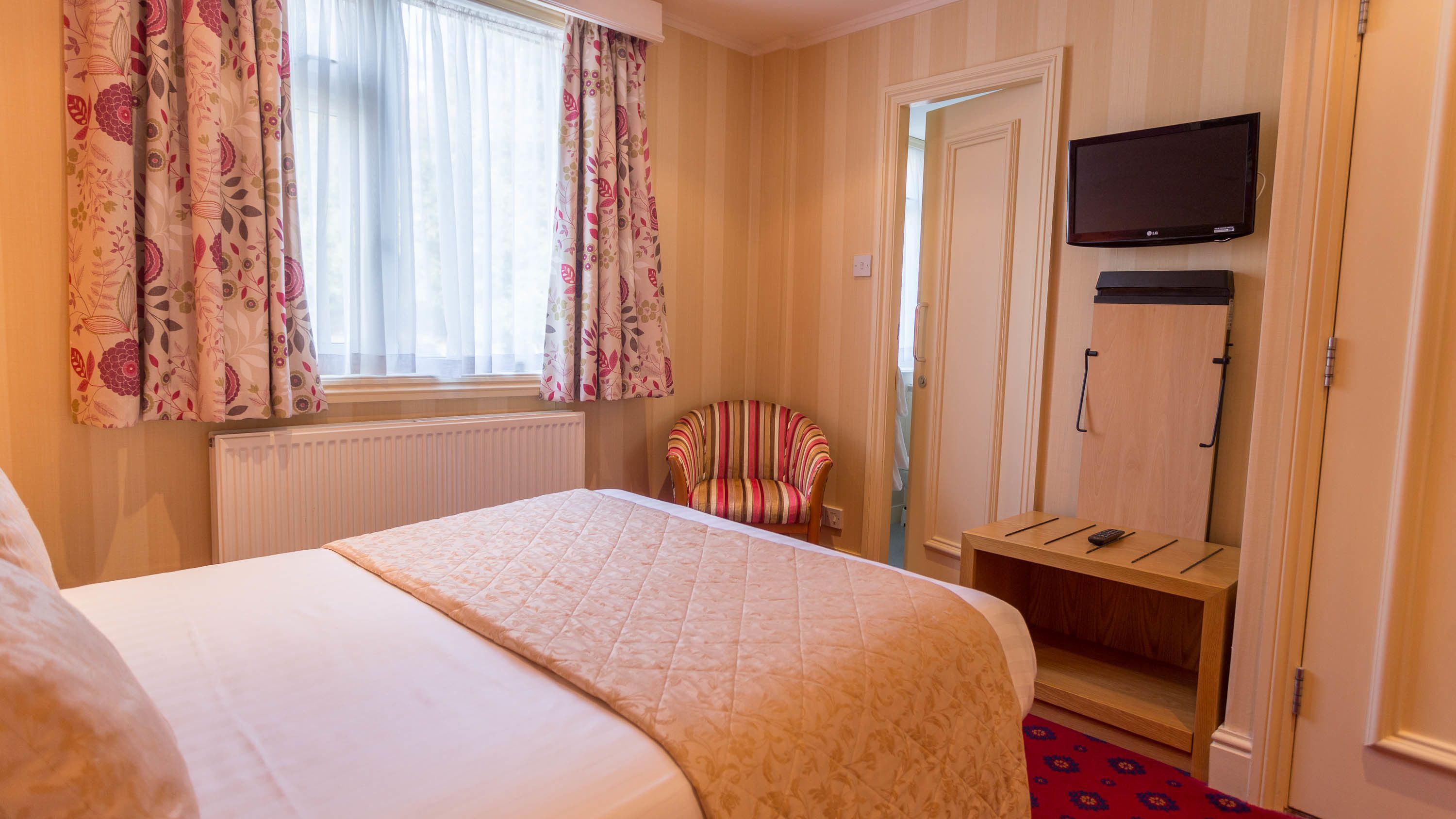A hotel room with a bed, a chair, a television, and a wardrobe.
