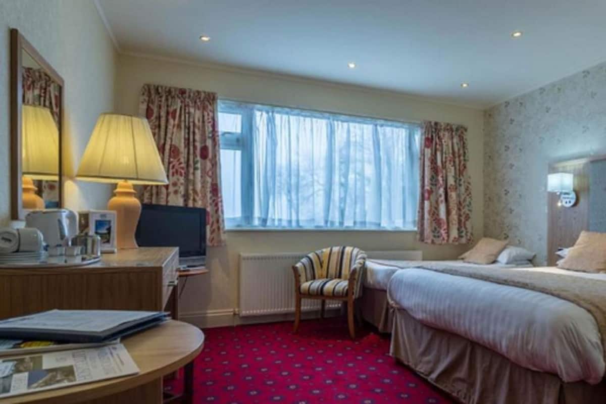 Habitación de hotel con cama, escritorio con lámpara, silla y ventana con cortinas.