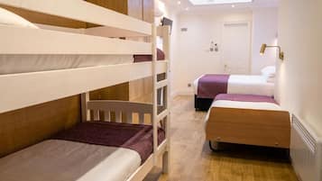 Habitación de hotel compacta con literas, un tragaluz, una puerta y una lámpara de noche.