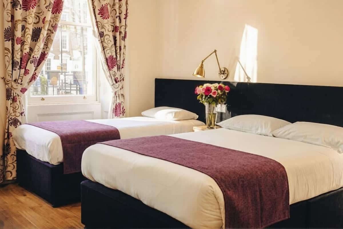 A hotel room with two beds, a nightstand, a lamp, and a window with curtains.