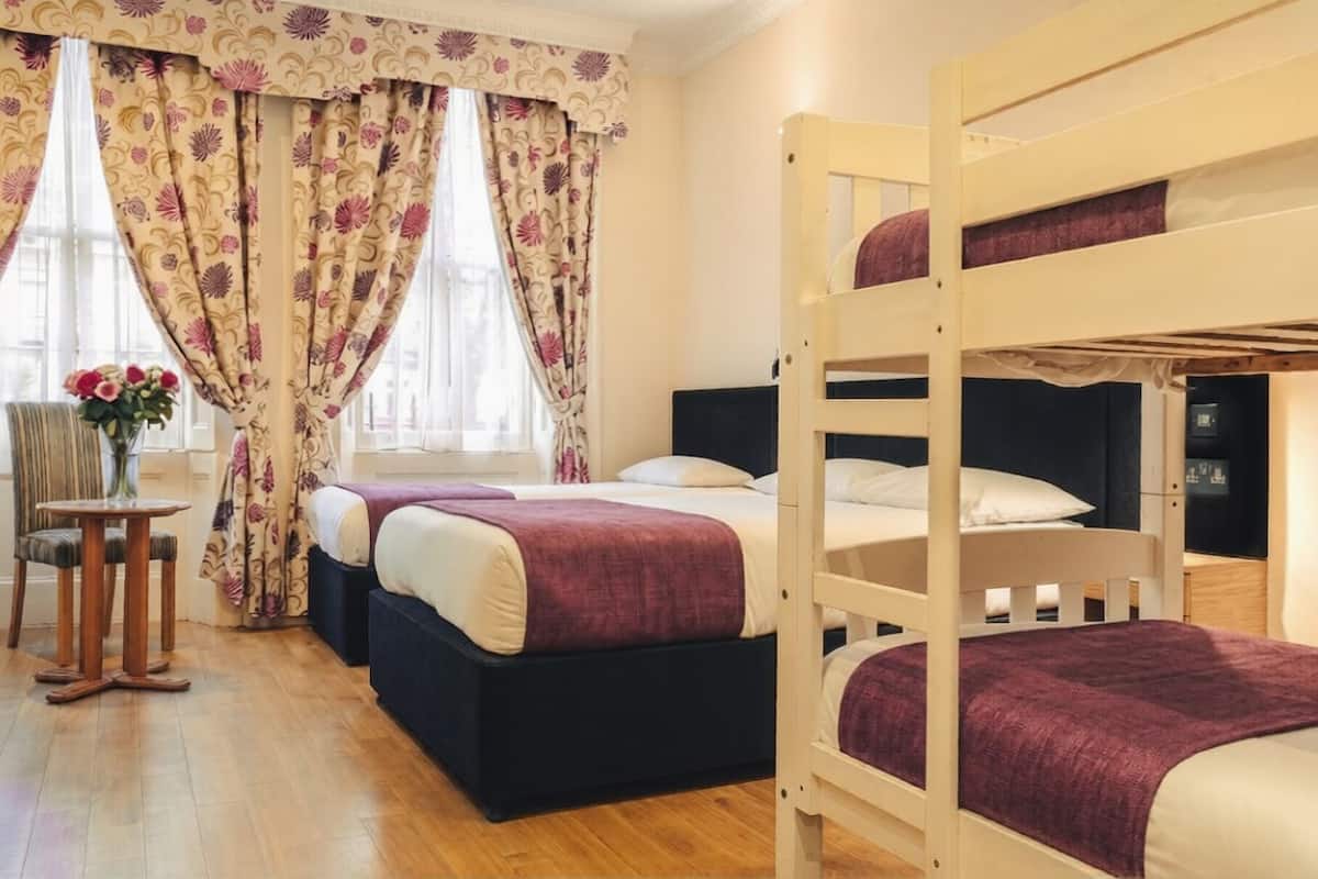 A room with bunk beds, a small table with a vase of flowers, and a window with curtains.