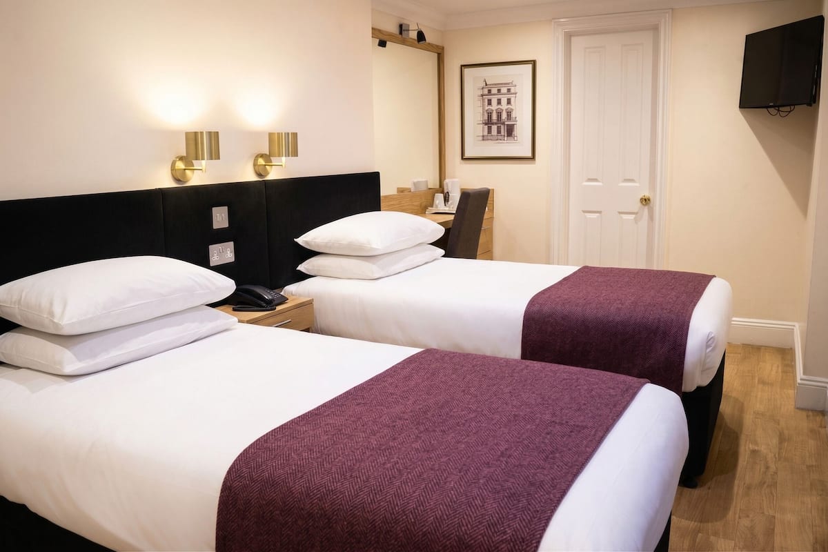A hotel room with two beds, a desk, a chair, a phone, and a framed picture on the wall.
