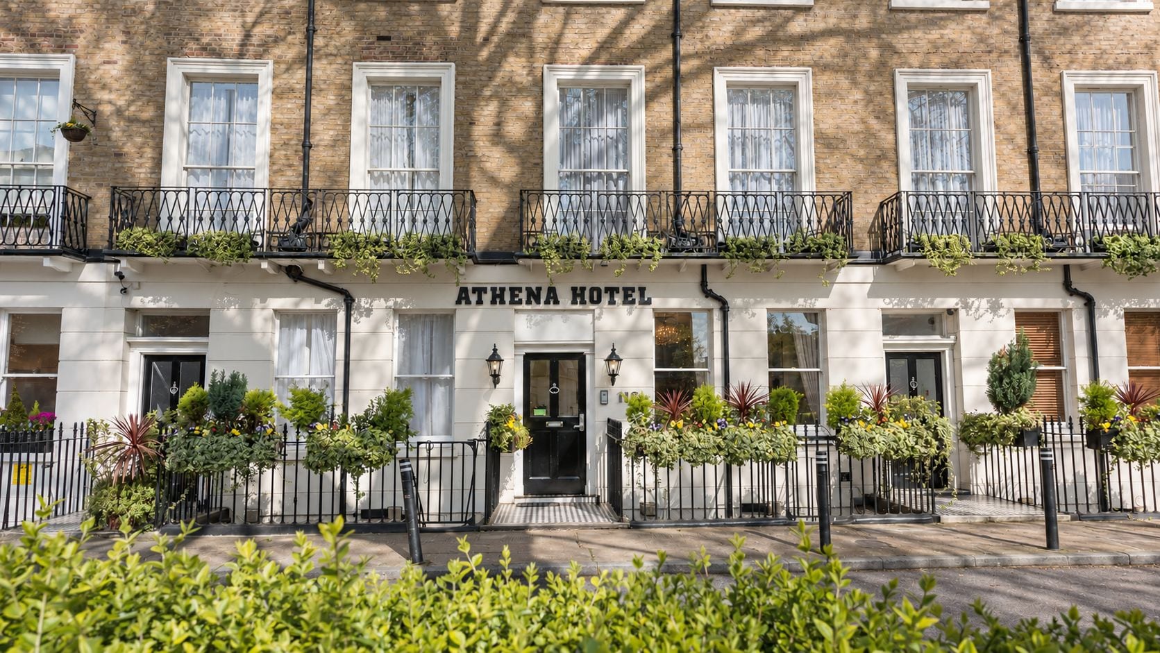 A hotel with a white facade, multiple windows, and a sign reading 'ATHENA HOTEL'.